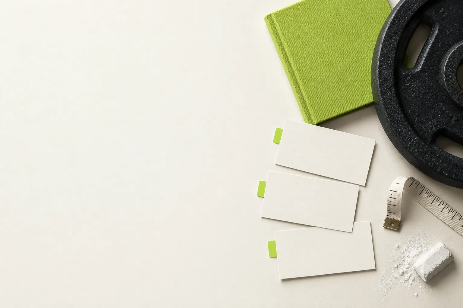 A weight plate, measuring tape, green notebook, and blank training cards on a pale surface.